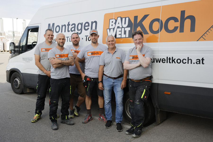 Sechs Männer der Firma Bauwelt Koch vor einem Firmenwagen in Wien.